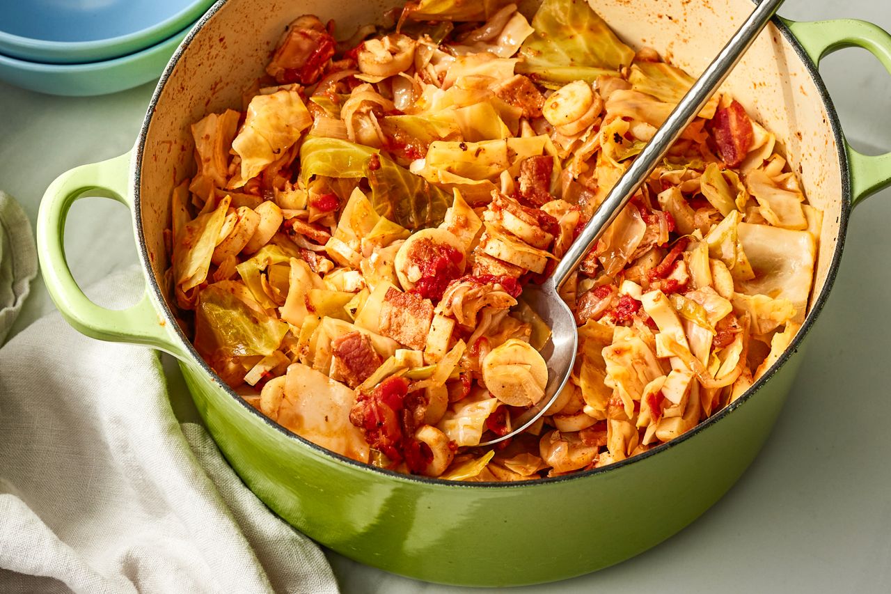 Angled view of a green dutch oven of swamp cabbage with a metal serving spoon
