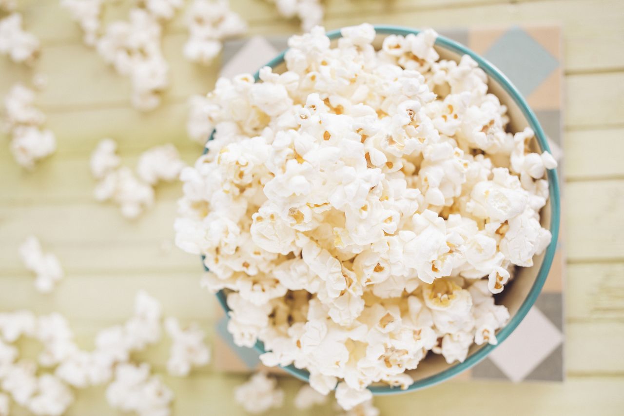 A bowl of popcorn on a table with scattered kernels