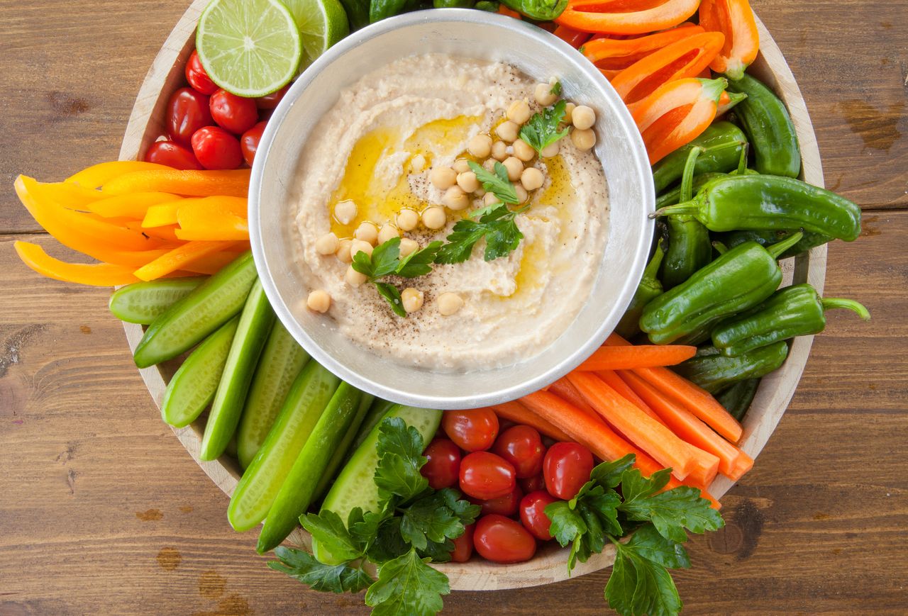 A platter of assorted fresh vegetables surrounding a bowl of hummus
