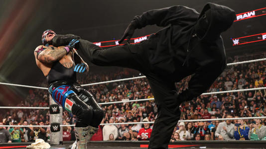 A masked figure superkicking Rey Mysterio