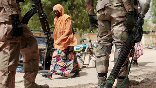 FILE - A woman walks past Nigerian soldiers at a checkpoint in Gwoza, northeast, Nigeria, April 8, 2015.