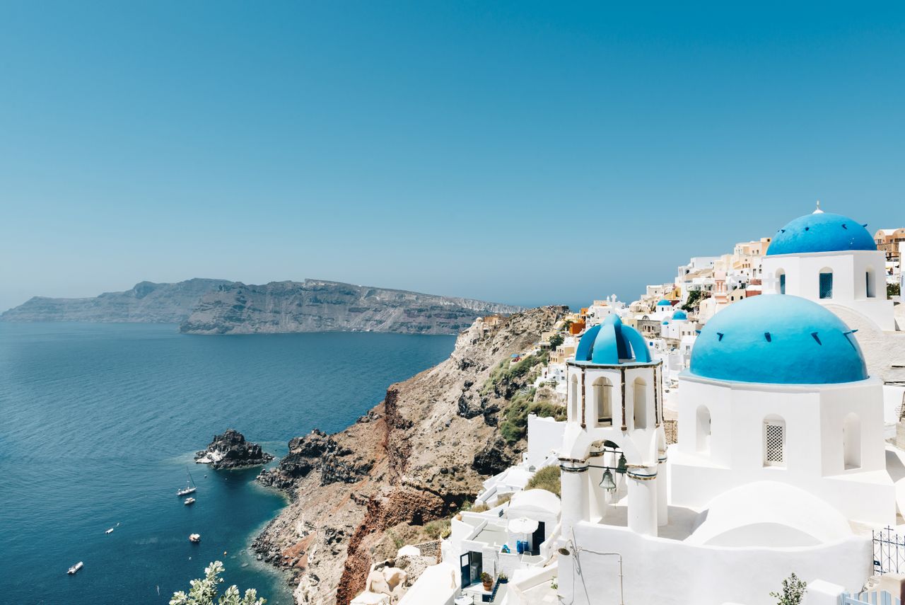 Coastal view of a Greek island with white buildings and blue domed roofs overlooking the sea