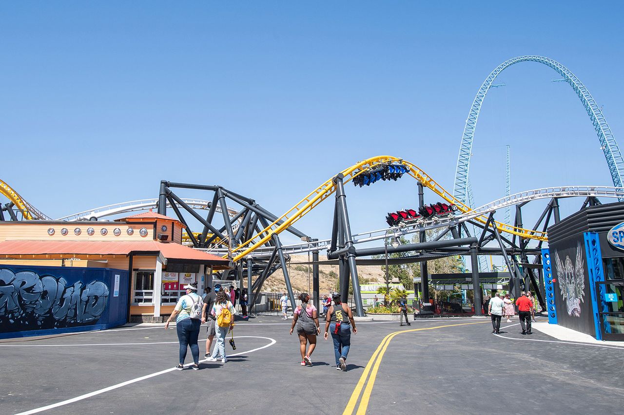 Visitors walk past the West Coast Racers roller coaster at the theme park Six Flags Magic Mountain on the day of the park's re-opening, April 1, 2021, in Valencia, California. - Six Flags Magic Mountain is the first theme park to re-open in Los Angeles County after closures amid the coronavirus pandemic.