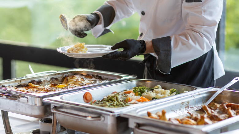 a person serves food from a buffet onto a plate