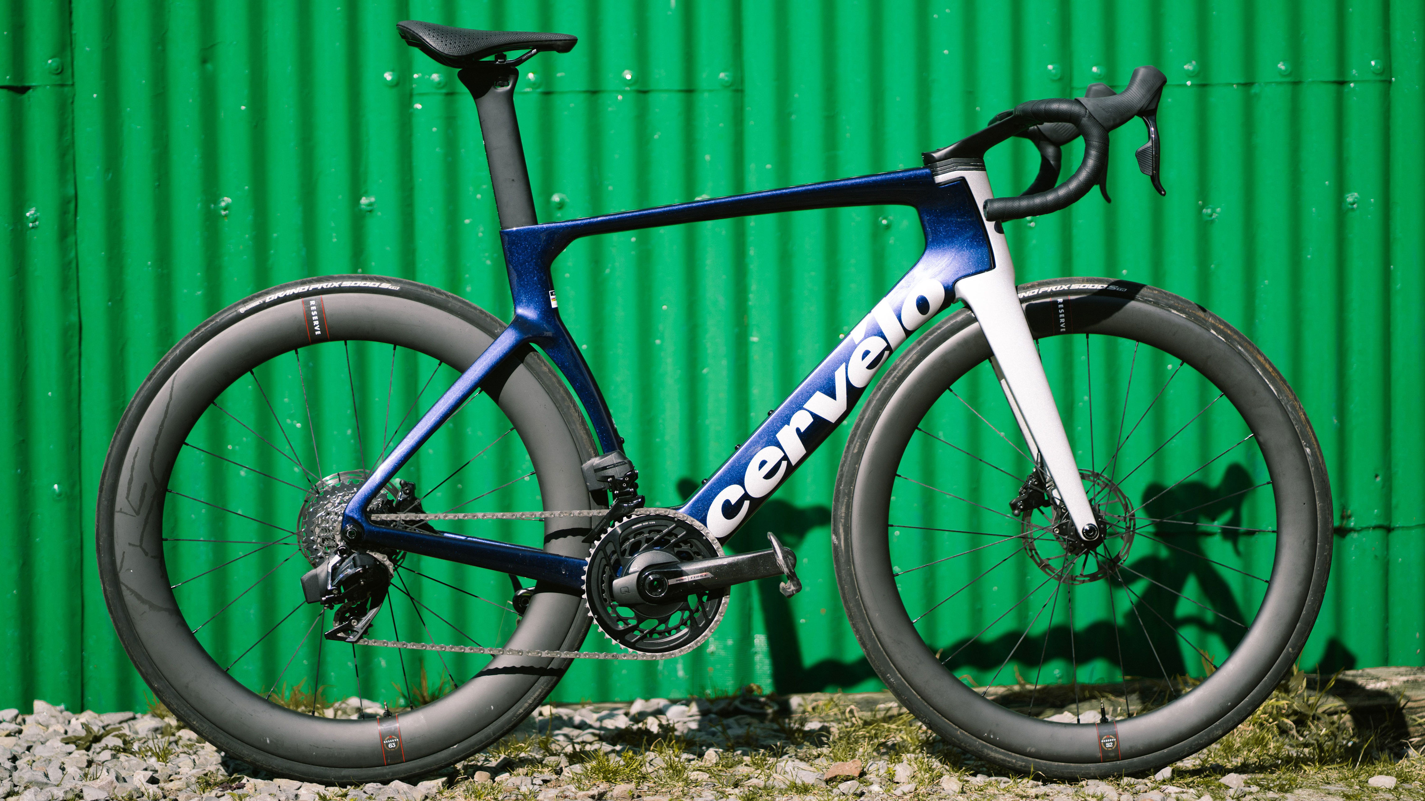 A purple road bike stands in front of a corrugated green metal wall.