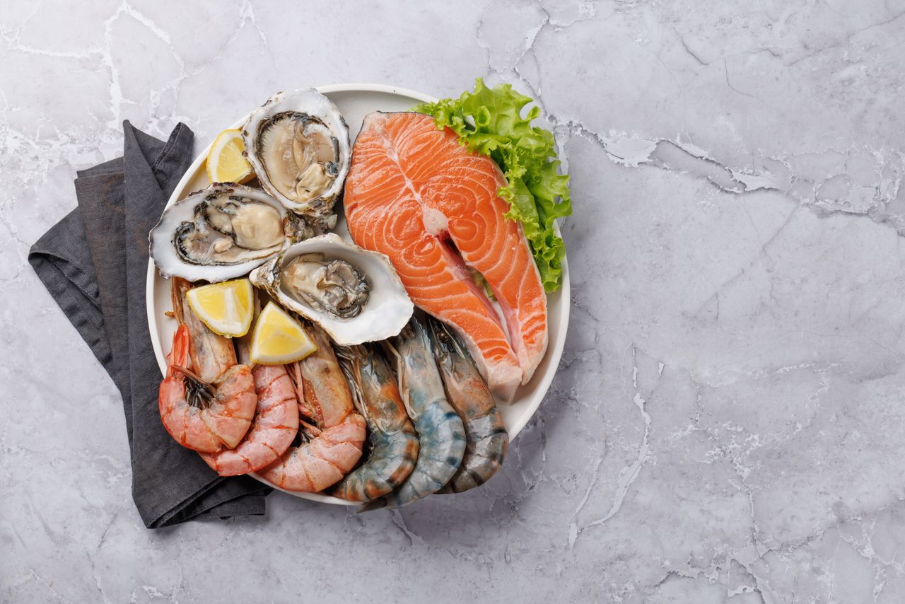 Plate with assorted seafood including shrimp, oysters, and a salmon steak served on a marble surface.