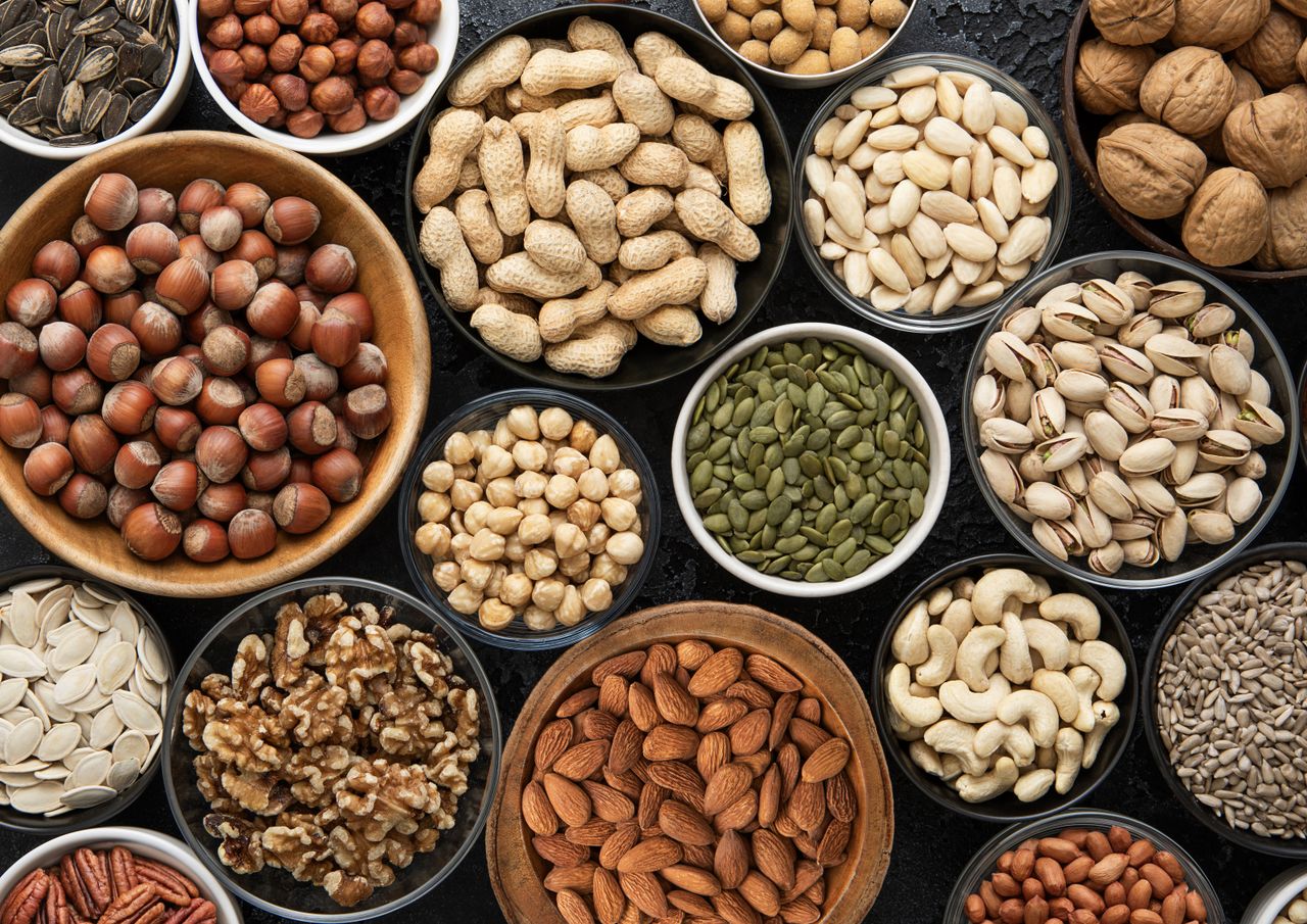 A variety of nuts and seeds arranged in bowls including hazelnuts almonds, walnuts, pistachios, and sunflower seeds.
