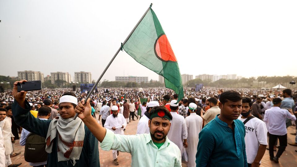 Mourners wave Bangladesh's national flag during the funeral of student leader Sharif Osman Hadi in Dhaka on December 20, 2025, after two days of violent protests over his killing. Huge crowds accompanied the funeral procession of Hadi, a key figure in last year's pro-democracy uprising who died in a hospital in Singapore on December 18 after being shot by masked gunmen while leaving a Dhaka mosque. (Photo by Niamul RIFAT / AFP)