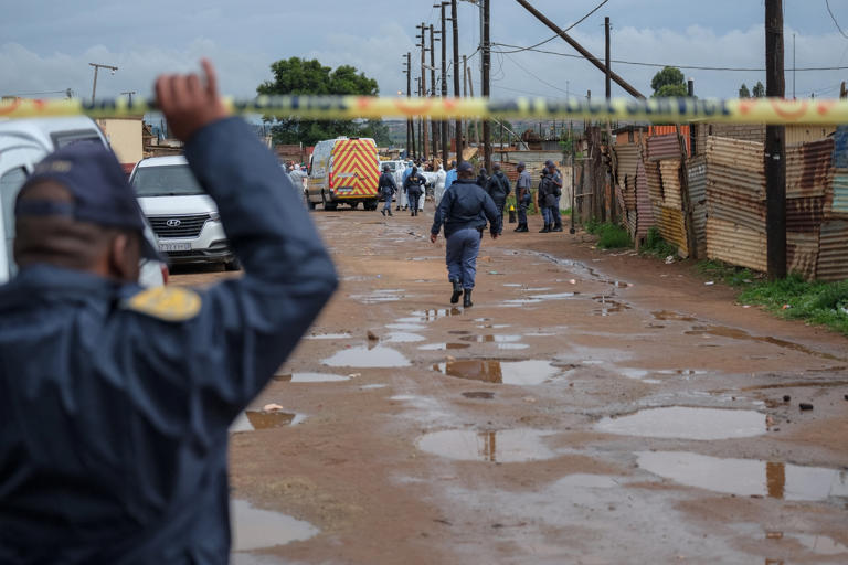 Emmanuel Croset/AFP via Getty Images - PHOTO: South African Police Service officers stand at the scene of an attack at a tavern in Bekkersdal on December 21, 2025. Nine people were killed when gunmen opened fire at a bar outside Johannesburg early on Dec. 21, 2025.