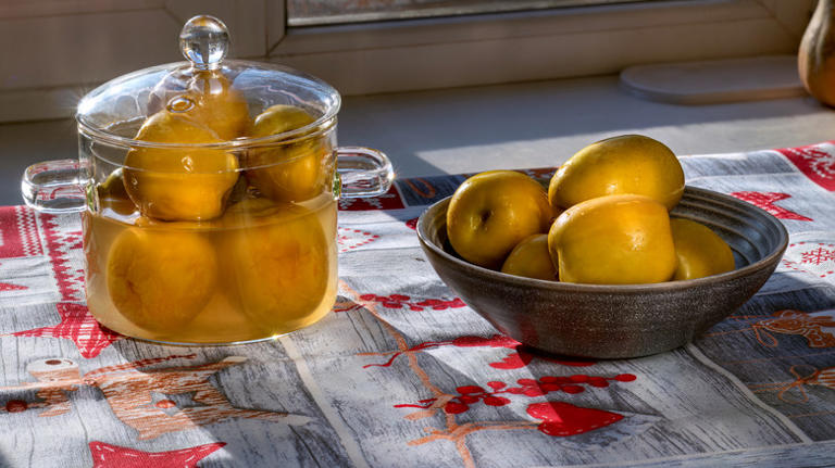 A bowl of yellow apples sitting next to a glass container of more apples that have been fermenting