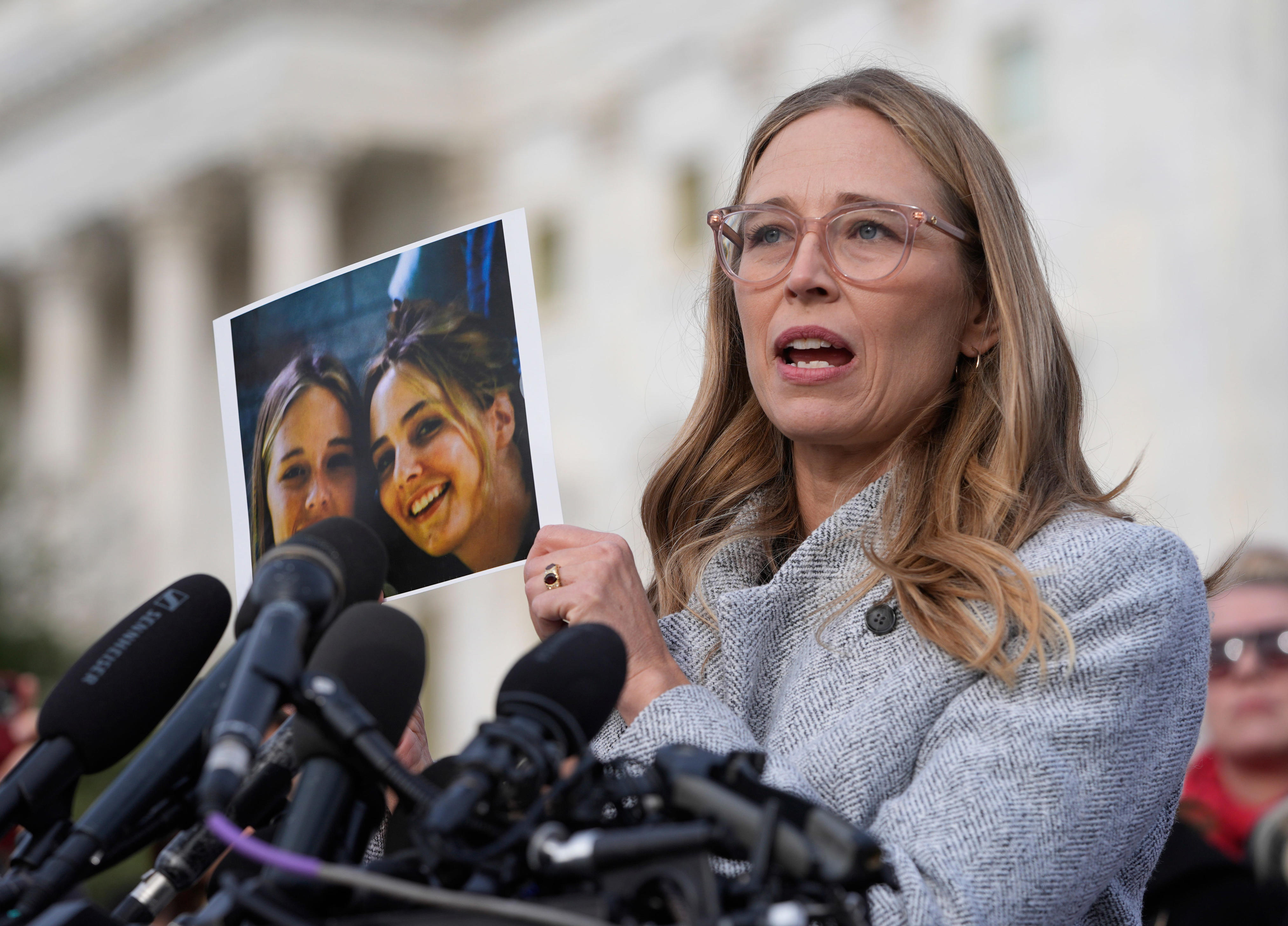 Annie Farmer, one of Maria Farmer's younger sisters, is seen in 2025 holding up a picture of them together when they were teenagers.