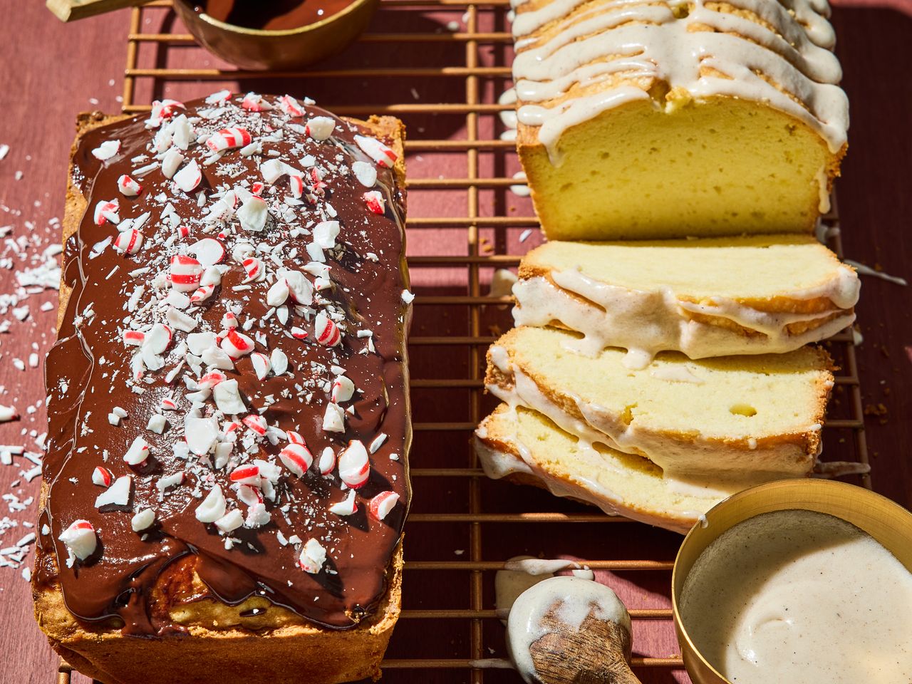 Two loaves of pound cake one topped with chocolate and crushed candy the other with glaze on a cooling rack