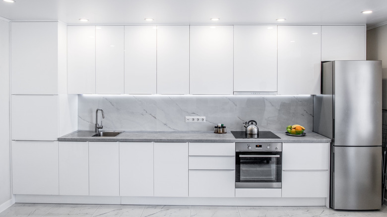 Front view of a modern white kitchen with many cabinets and silver appliances