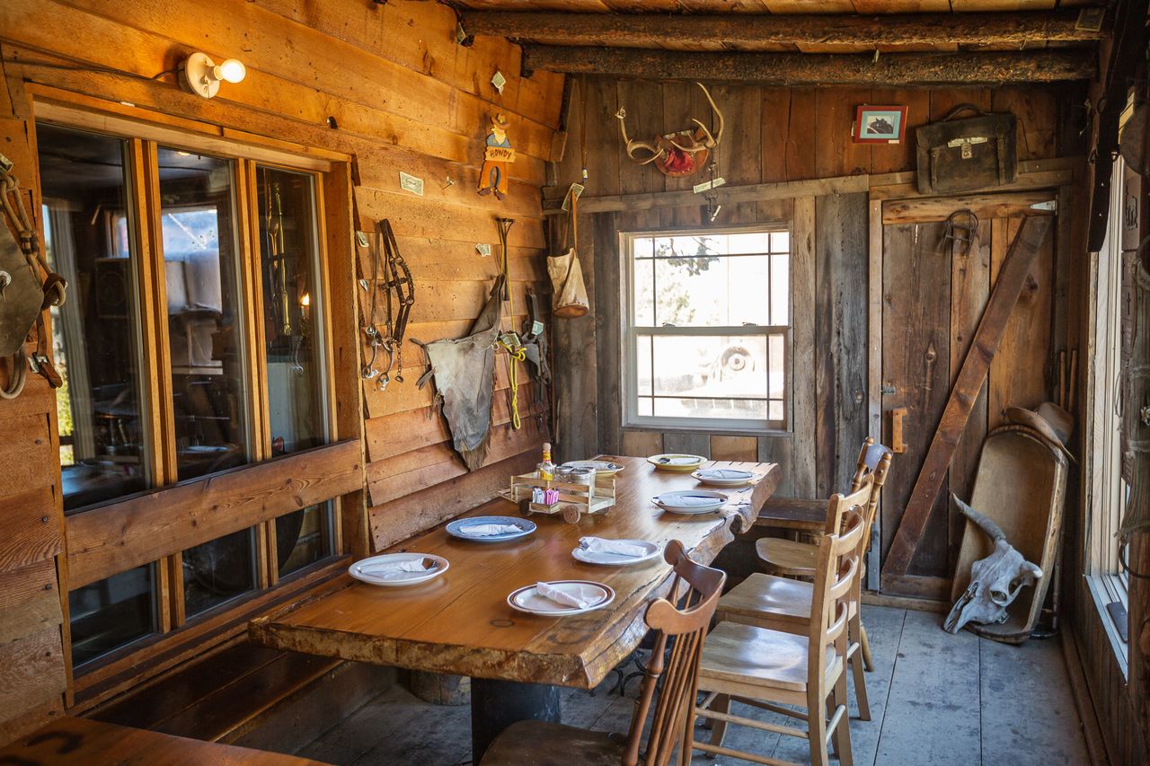 Rustic dining area with a wooden table set for a meal located inside a cabinstyle room with wooden paneling and decorations