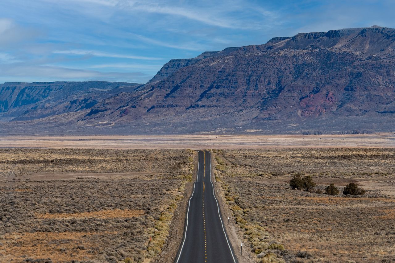 A straight road leading through a flat landscape toward distant mountains