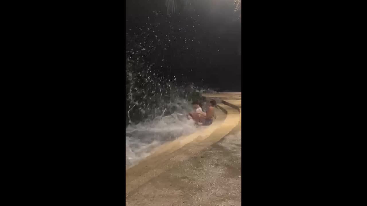 Wave crashes into friends as they sit together on beach steps