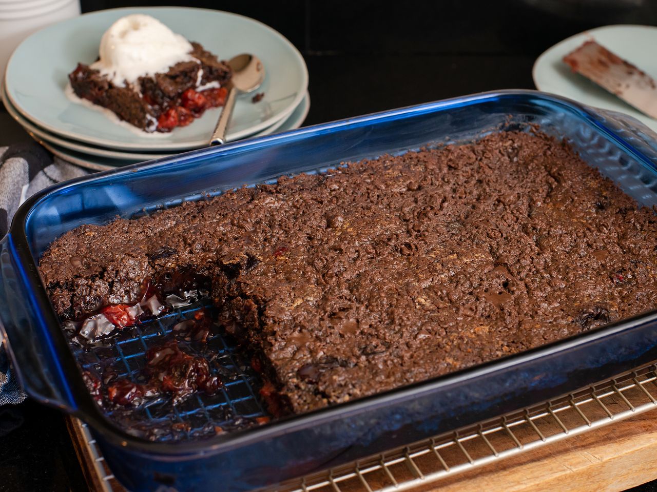 a high angle view looking over the edge of a blue glass 9x13 baking dish into a black forest brownie dump cake with a slice removed and plated in the background.