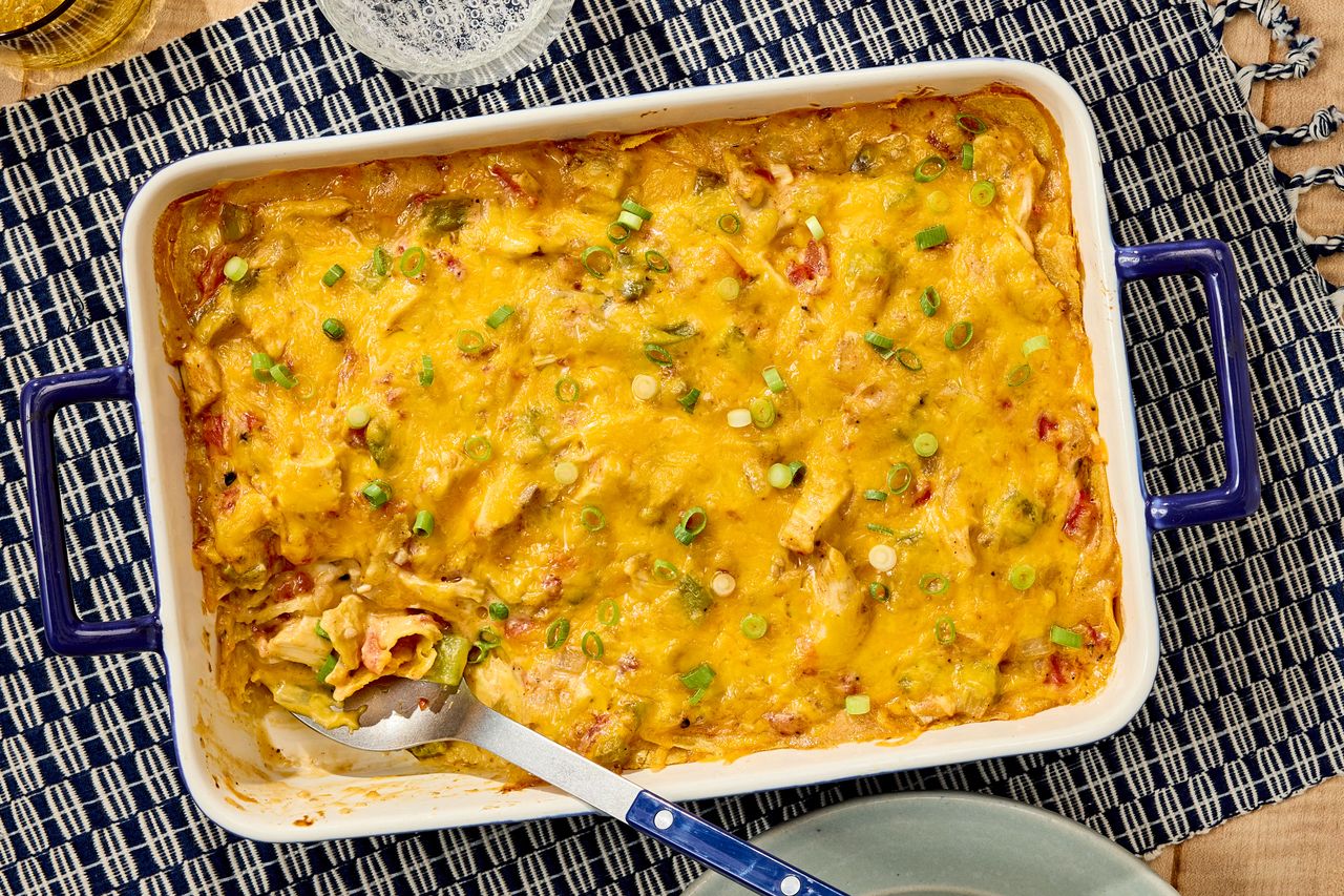 Baked chicken casserole topped with melted cheese and garnished with green onions served in a rectangular dish with a serving spoon