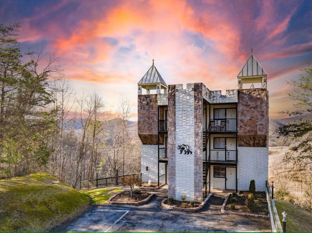 A condo building that has had a medieval makeover with tall spireing towers amidst a brilliant mountainous landscape.