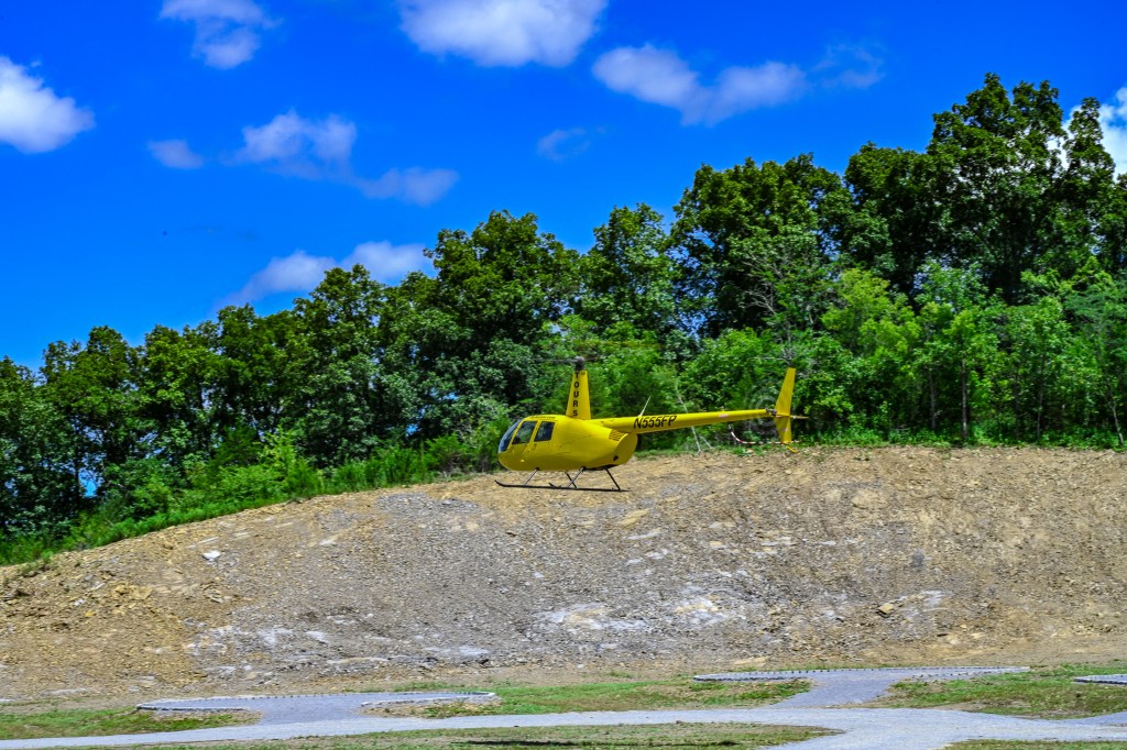 A small yellow helicopter is taking off from the helipad ready for an epic and scenic adventure.