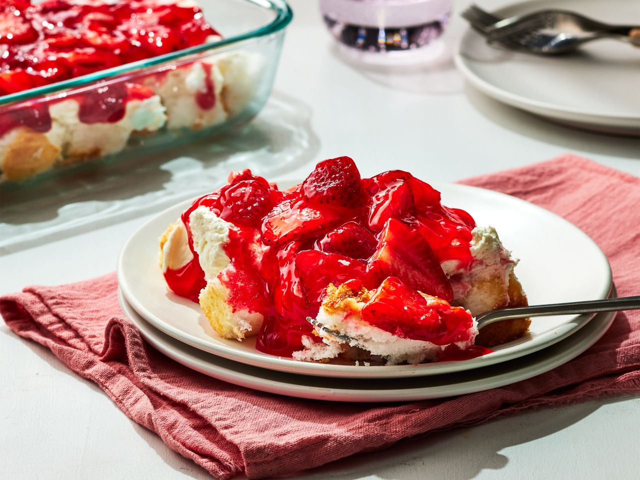 A plate of strawberry angel food dessert, with a glass dish of strawberry angel food dessert in the background