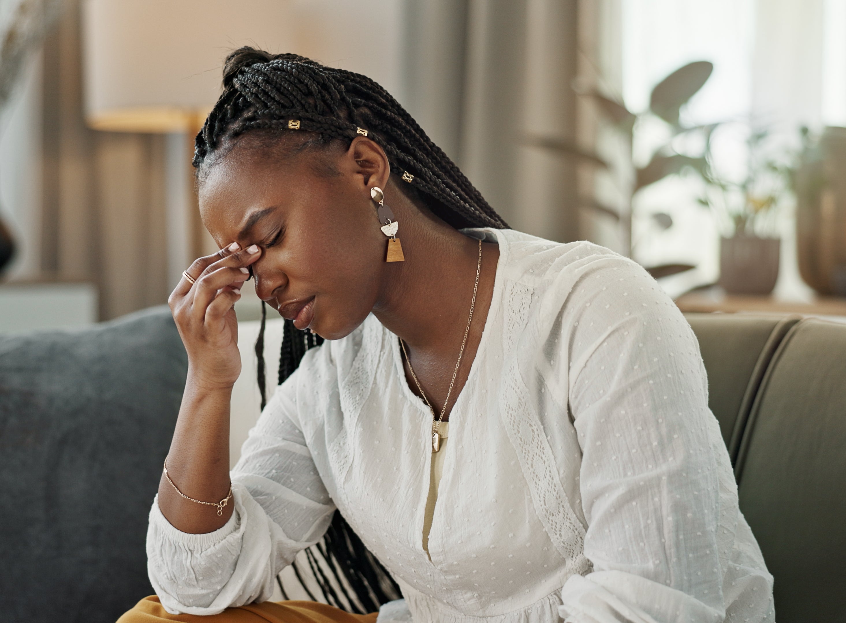 A person sitting on a couch, wearing a white top, appears stressed or upset, with one hand on their forehead