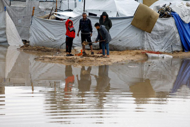 Displaced Palestinians stand near accumulated rainwater as they shelter in a flooded tent camp on a rainy day in Nuseirat, central Gaza Strip, December 12, 2025. REUTERS/Mahmoud Issa