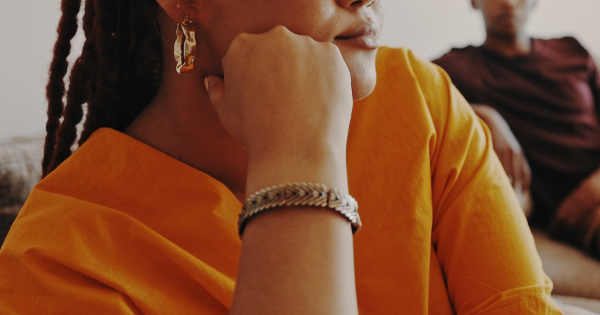Woman in thoughtful pose on a couch, with a man sitting in the background. Scene suggests a moment of relationship reflection