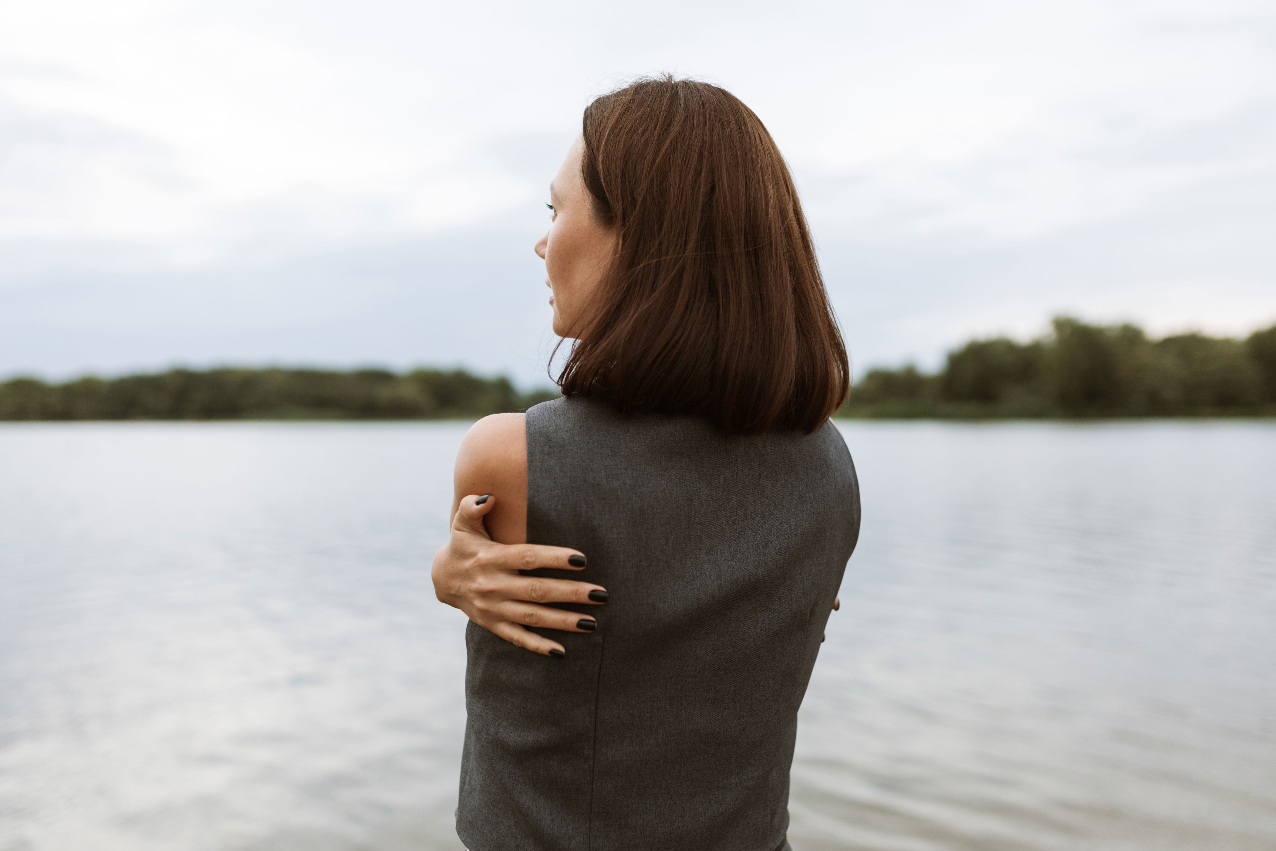Woman by a lake, seen from behind, hugging herself