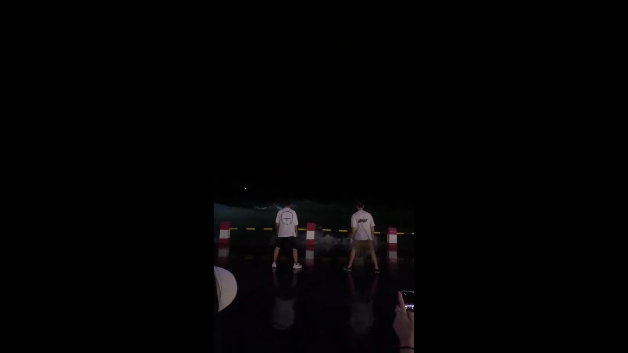 Two men perform synchronized jump moves as wave crashes in Guangxi
