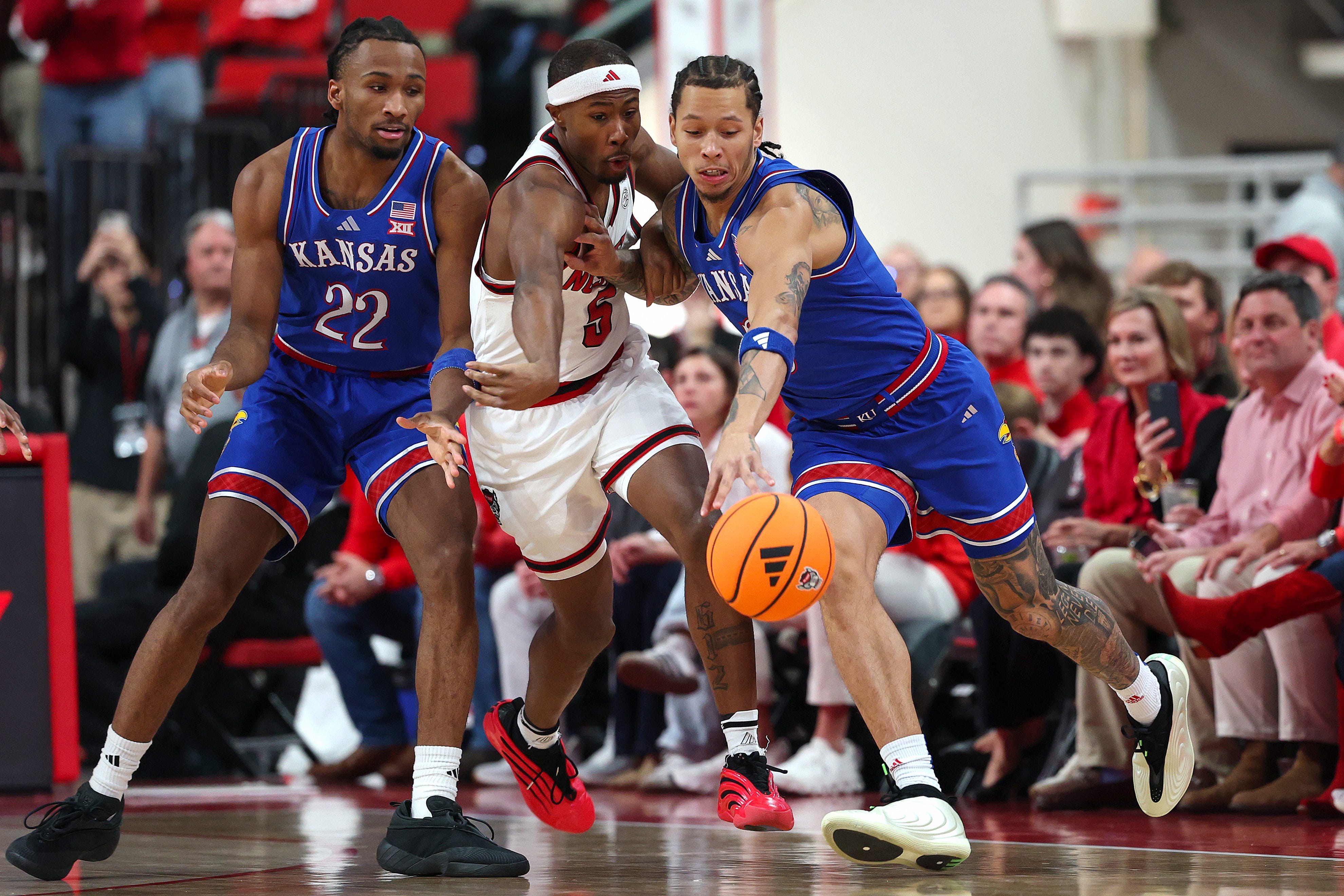 RALEIGH, NORTH CAROLINA - DECEMBER 13: Tre Holloman #5 of the NC State Wolfpack defends a pass from Tre White #3 to Darryn Peterson #22 of the Kansas Jayhawks during the first half of the game at Lenovo Center on December 13, 2025 in Raleigh, North Carolina. (Photo by Grant Halverson/Getty Images)