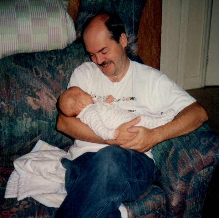 A man holding a baby in his arms while sitting on a couch, smiling affectionately at the baby