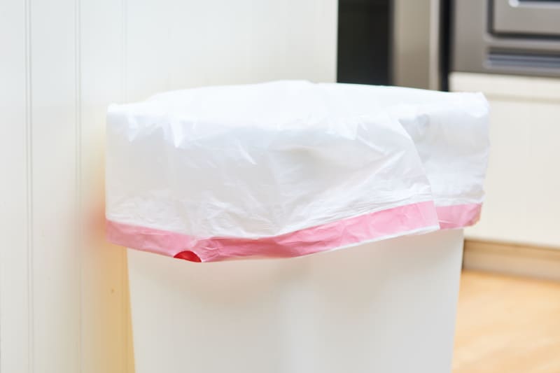 White trash can with a pink-tinted liner in a kitchen setting.