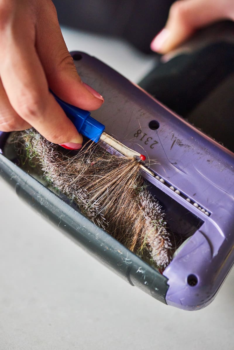 Hand using a seam ripper to remove hair from a vacuum brush roll.