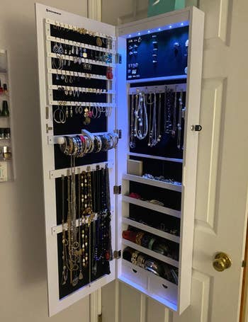 Jewelry organizer mounted onto the wall and opened to show jewelry organized inside and light on