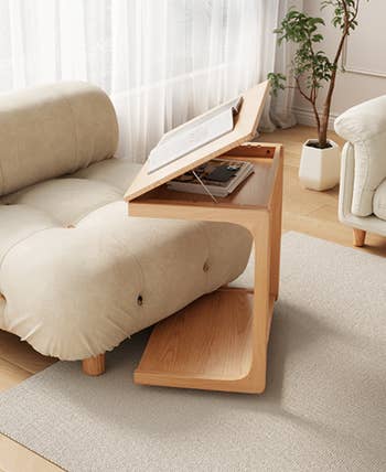 Adjustable wooden side table with open book, featuring a modern Z-shape design beside a cozy sofa in a bright, airy living room