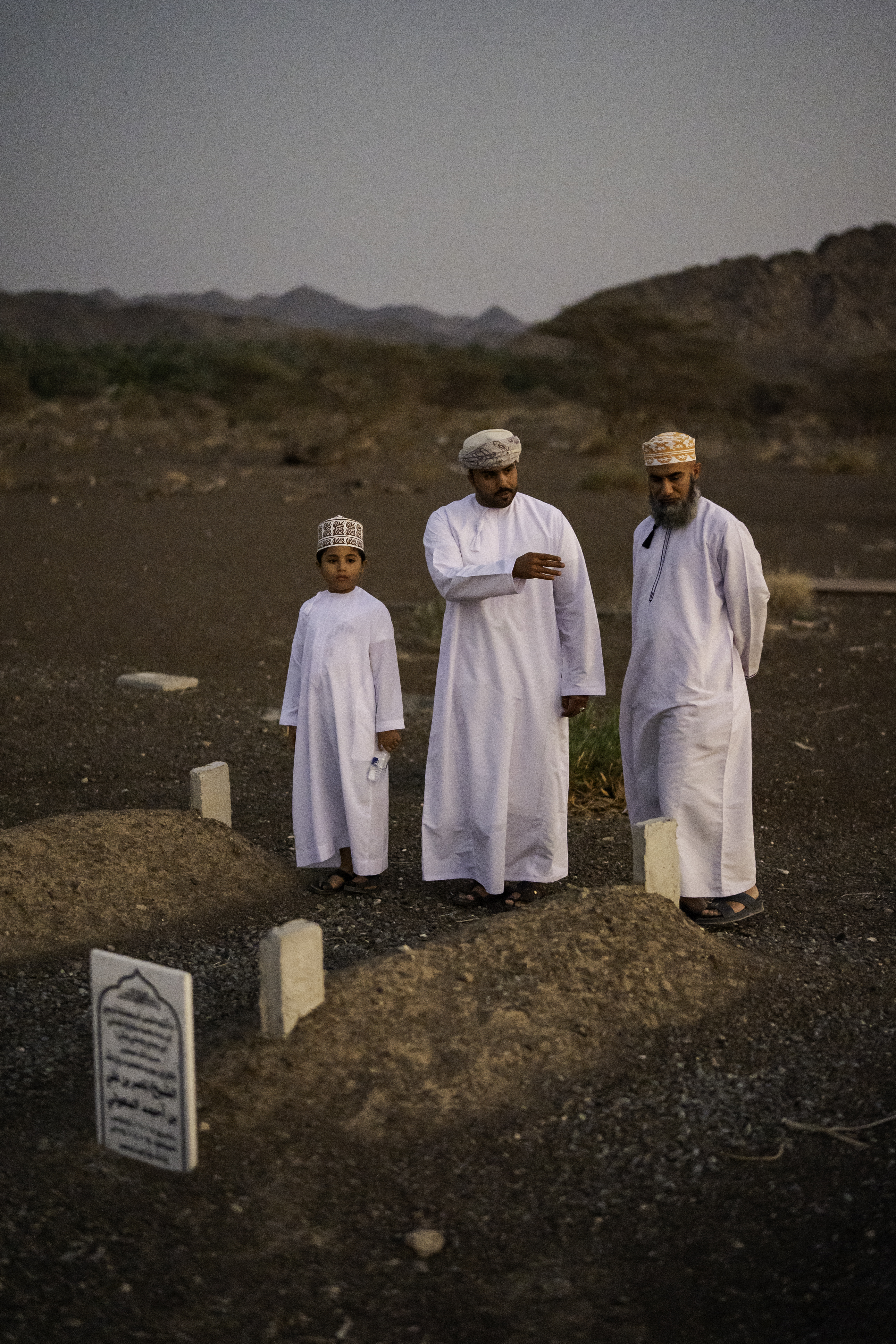 Yousuf Mawaly, right, with his nephew Yahya al-Mawaly and his son Saif al-Mawaly, 9, at the cemetery to visit the two sheikhs who lost their lives during the flood in Samad al-Shan.