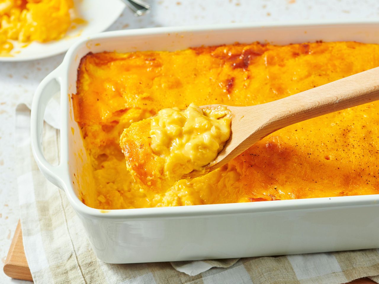 A dish of baked mac and cheese with a wooden spoon scooping a portion