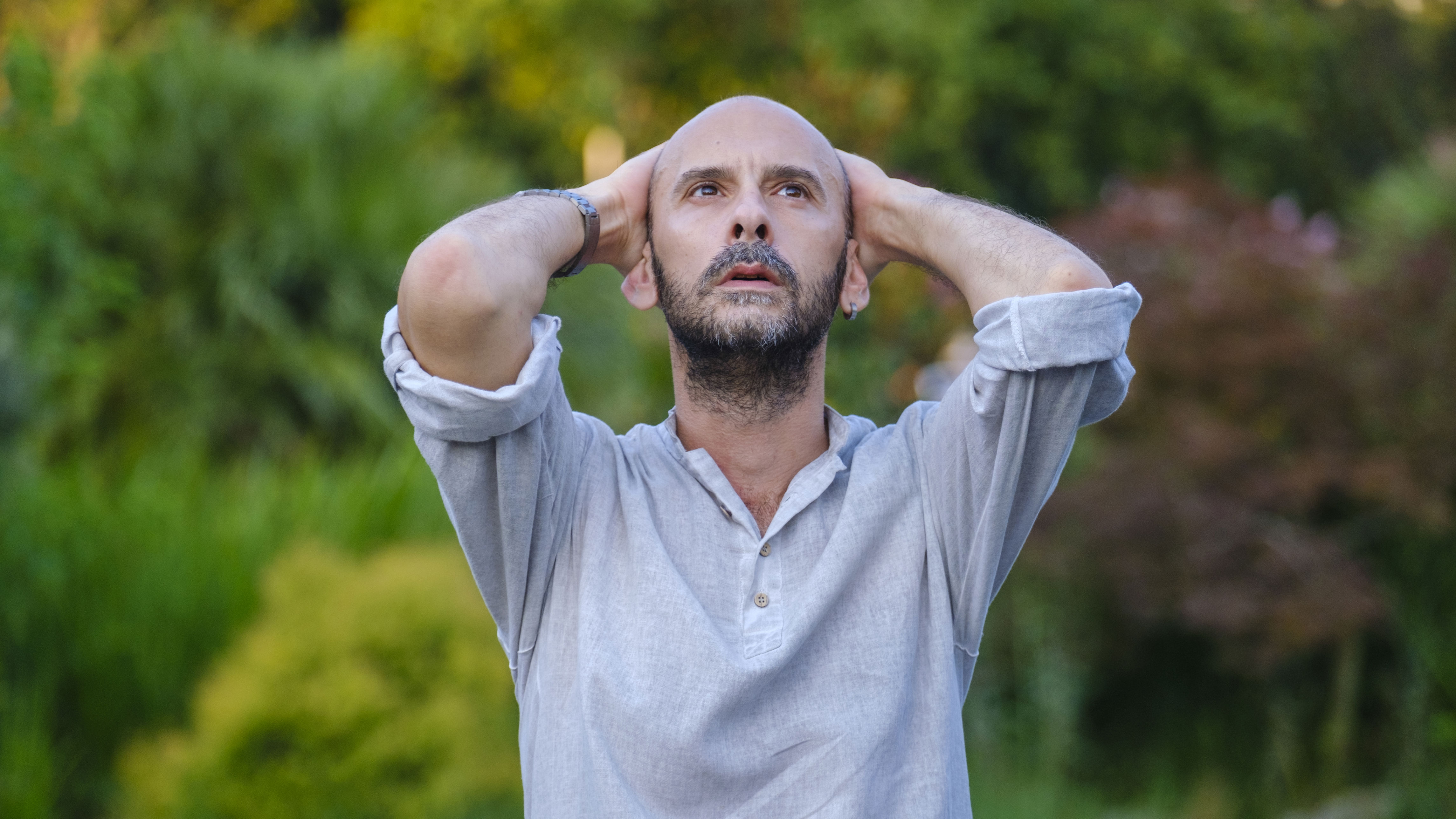 A middle-aged handsome businessman in a park, with his hands on top of his head, expressing a moment of distress and sadness