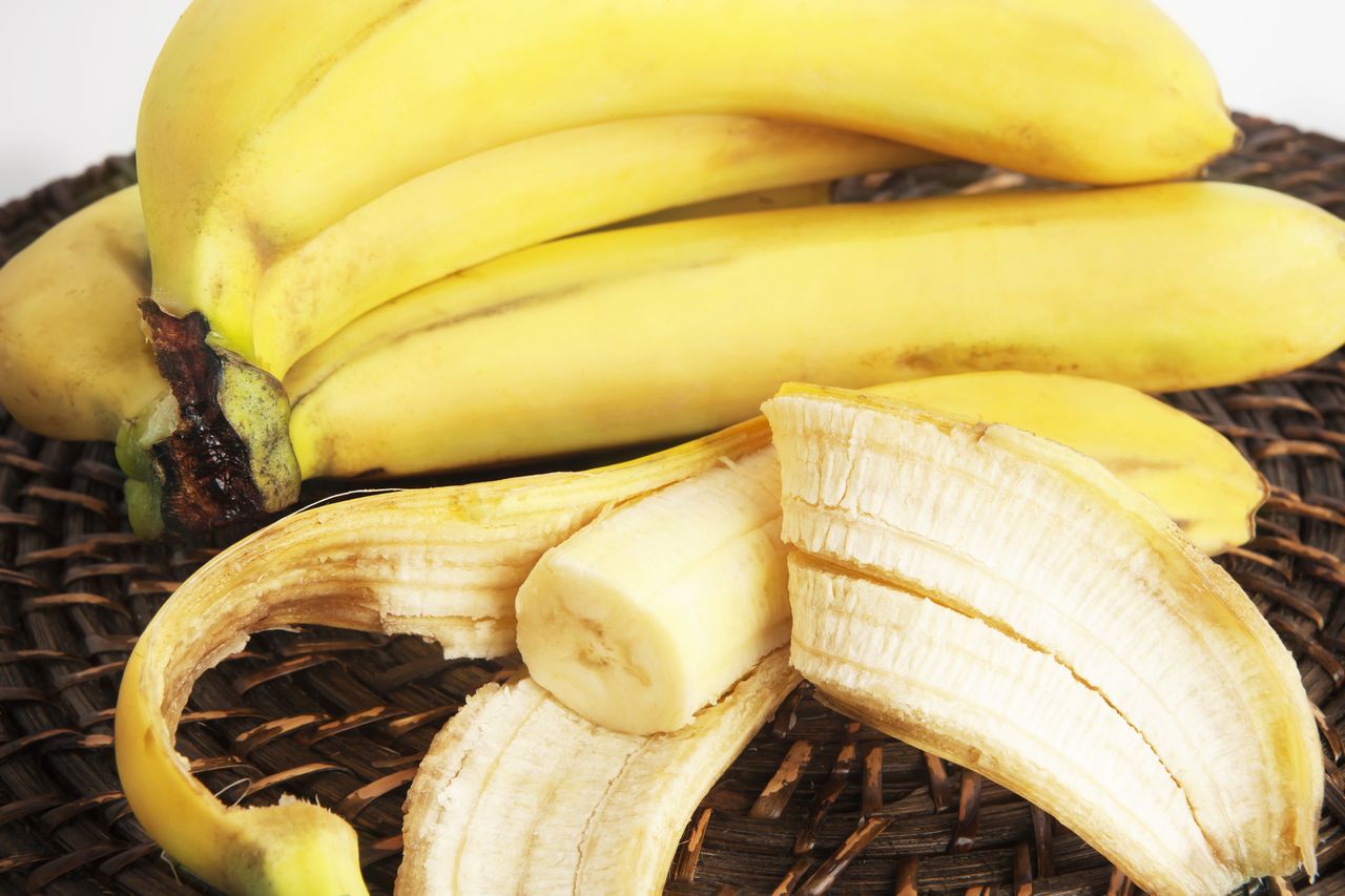 One peeled banana and bunch of bananas on wicker surface.