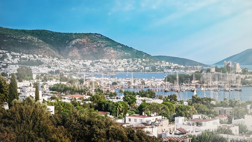Coastal town with ancient architecture and marina, depicting scenes related to the forgotten 7 wonders of the ancient world.