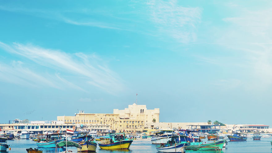 Colorful boats anchored in front of an ancient fortress, showcasing the forgotten 7 wonders of the ancient world in their prime.