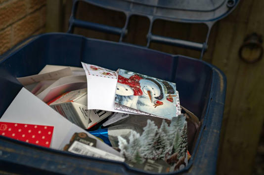 A blue storage bin filled with a variety of items, including bundled mail, assorted printed materials, and a decorative object.