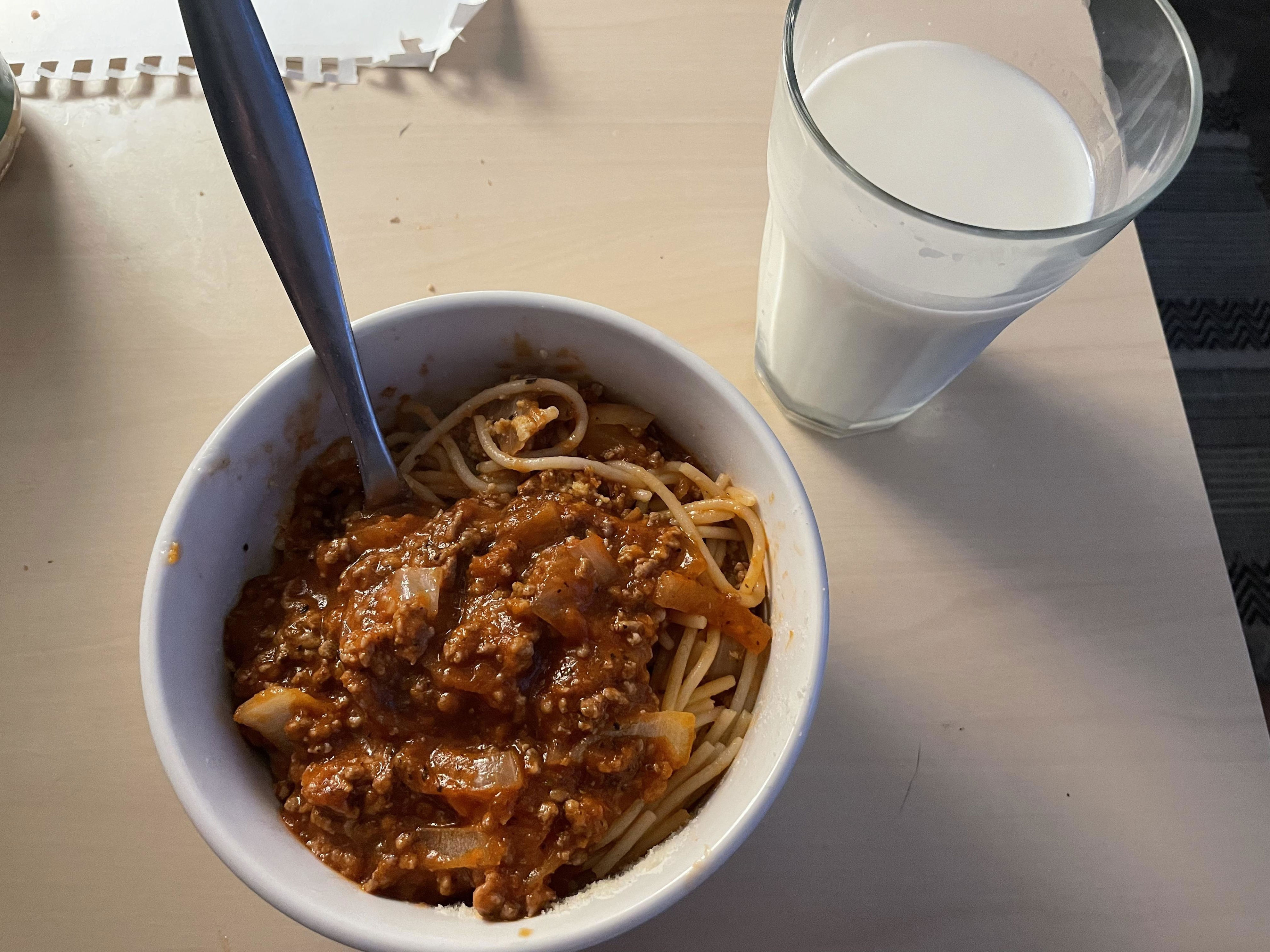 A bowl of spaghetti Bolognese with a glass of milk on the side