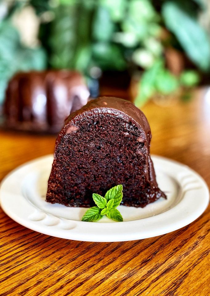 a slice of dark chocolate Bundt cake on a white plate garnished with a mint sprig