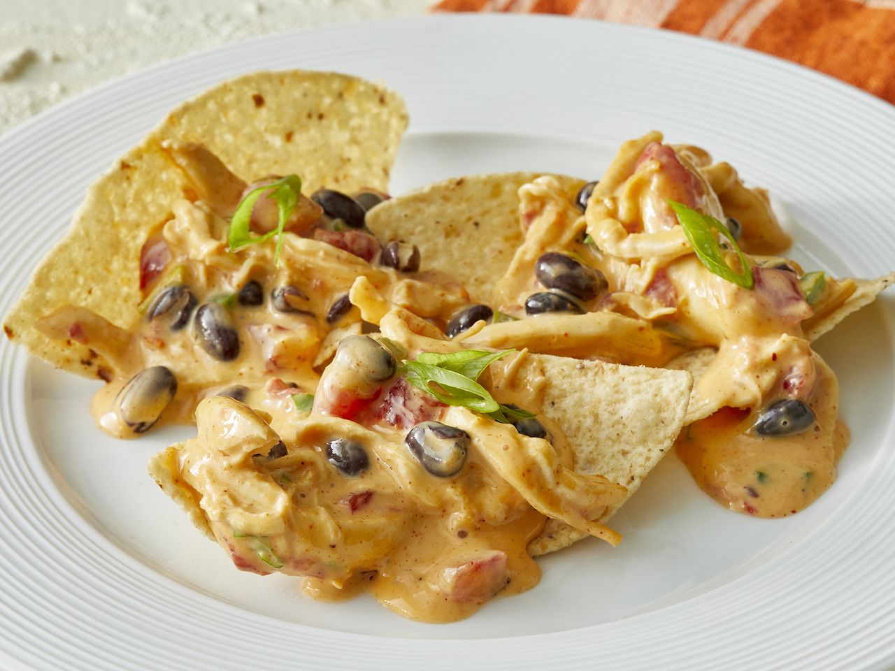 high angle looking at a place of tortilla chips, topped with chicken nacho dip with black beans and green onions