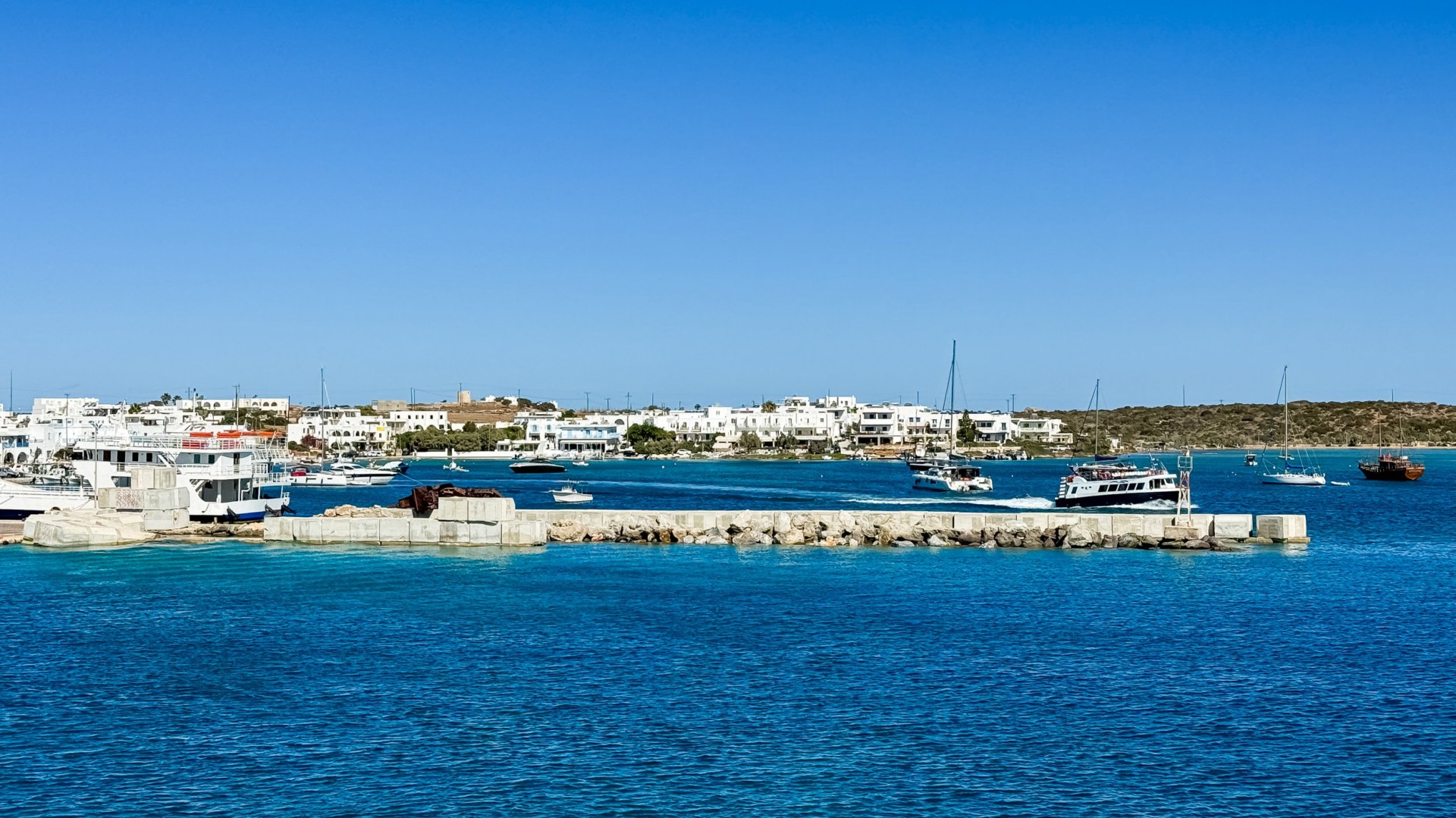 A small town white white buildings viewed from out at sea, under a blue sky.