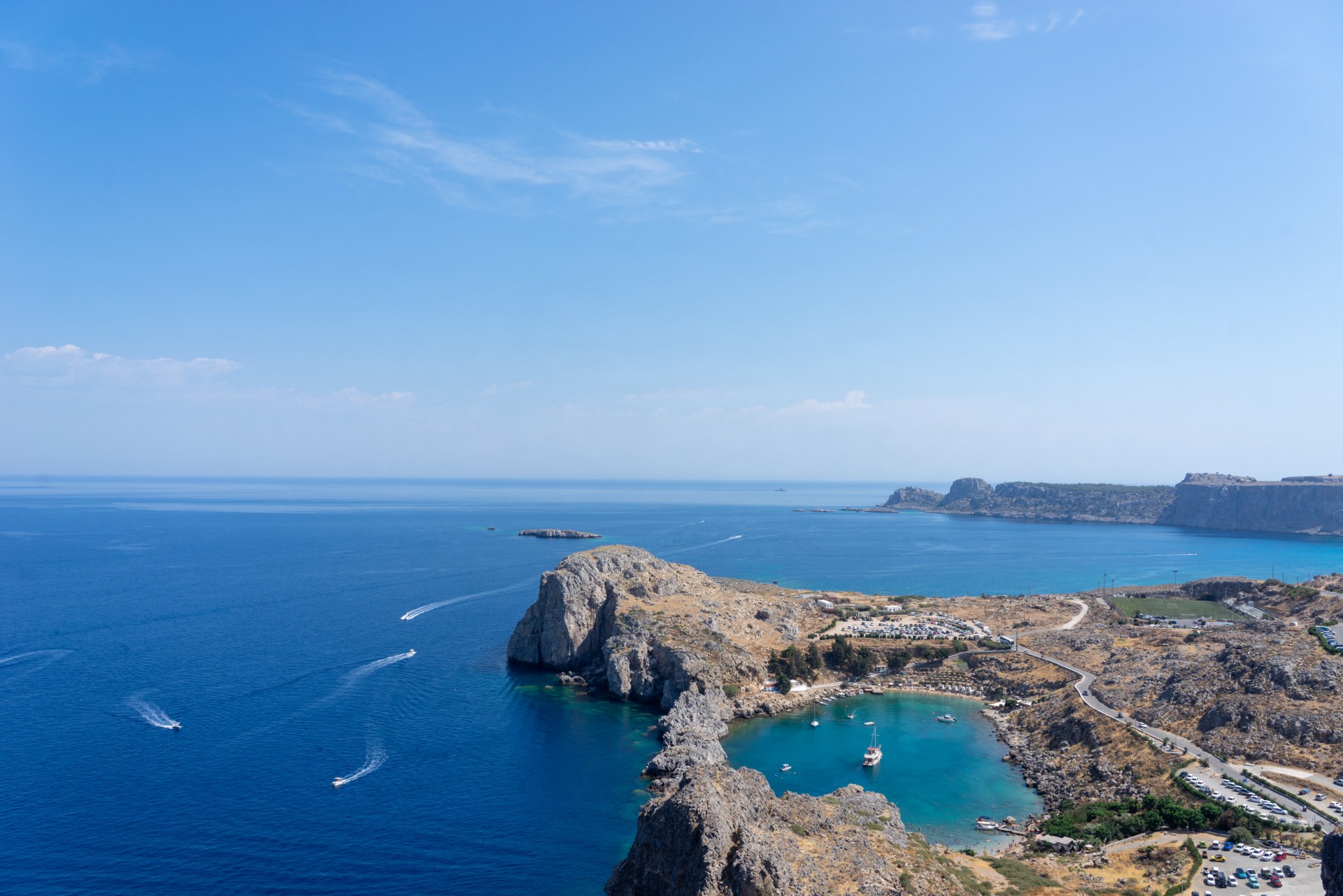 A rocky outcrop with a secluded pool in the middle surrounded by the ocean under a blue sky.