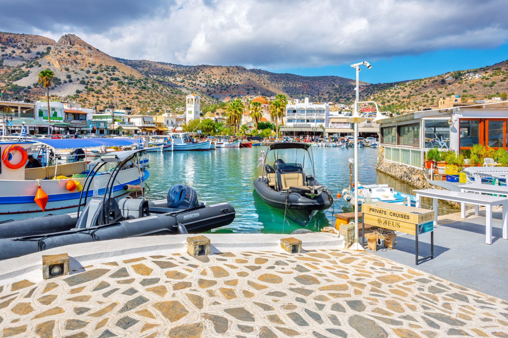 Colorful fishing boats in a cobbled marina with hills across the water in the distance.