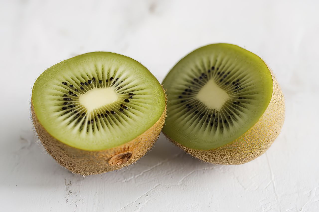 A fresh kiwi sliced in half on a white stone tabletop.